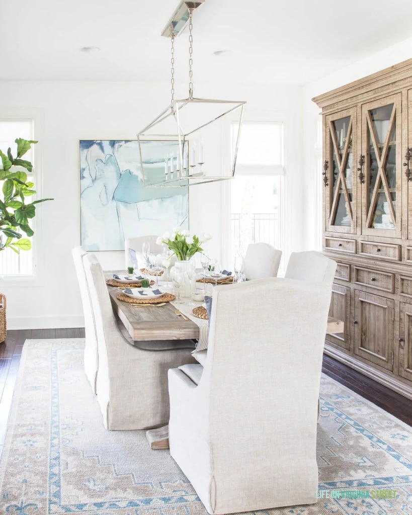 A spring dining room with an Easter tablescape. I love the neutrals mixed with blues and greens. The linen chairs and wood dining table pair perfectly with the more modern chandelier!