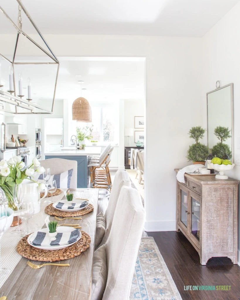 A coastal inspired Easter tablescape with linen chairs, reclaimed wood dining table, navy blue and white striped napkins and pillows, water hyacinth chargers and more! Such pretty spring decorating ideas!