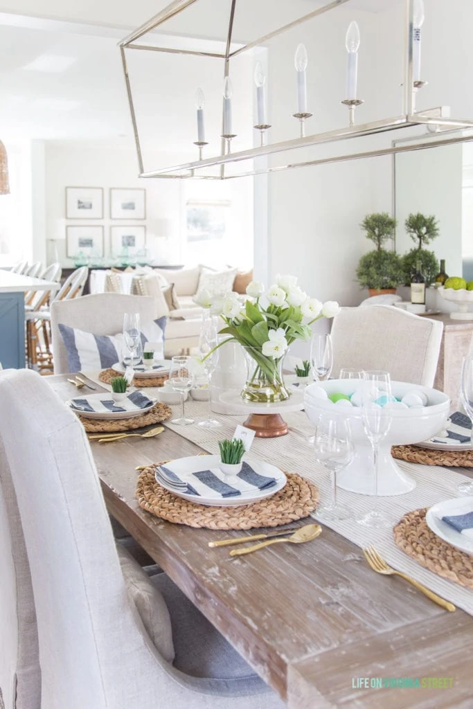 An Easter tablescape with navy blue and white stripes, gold flatware, sisal chargers, white tulips and more!