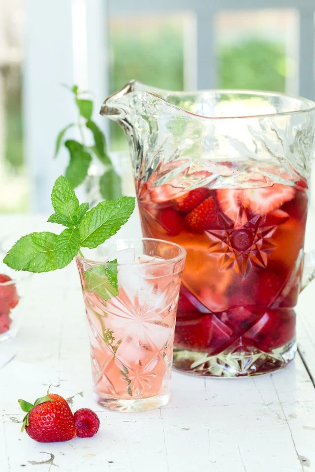 Strawberry Raspberry Rose Sangria in a pitcher and a glass is poured with a sprig of mint inside the cup.