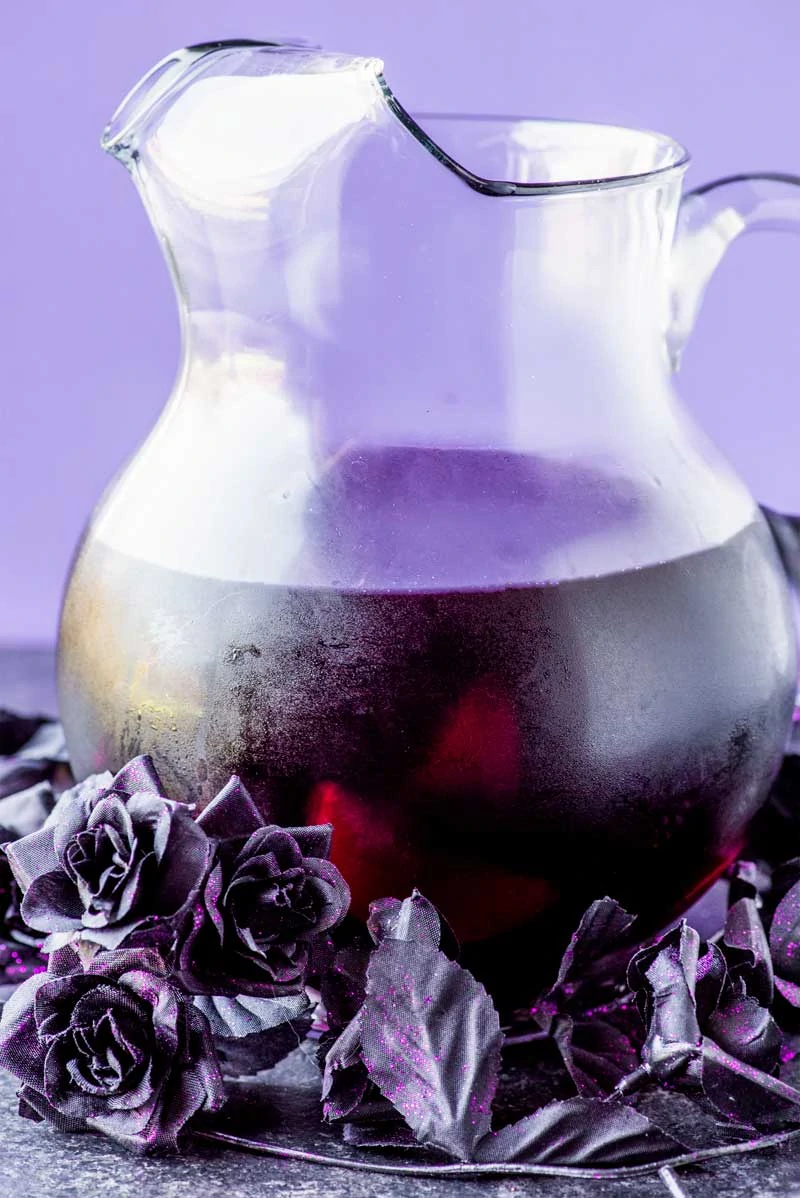 Black Magic Sangria which is dark purple in color ad a dark purple flowers surrounding the jug.