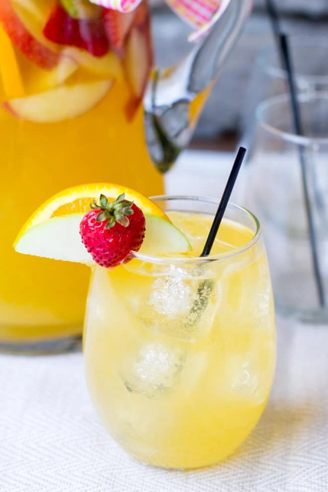 A passion fruit sangria with a strawberry and an orange on the rim of the glass.