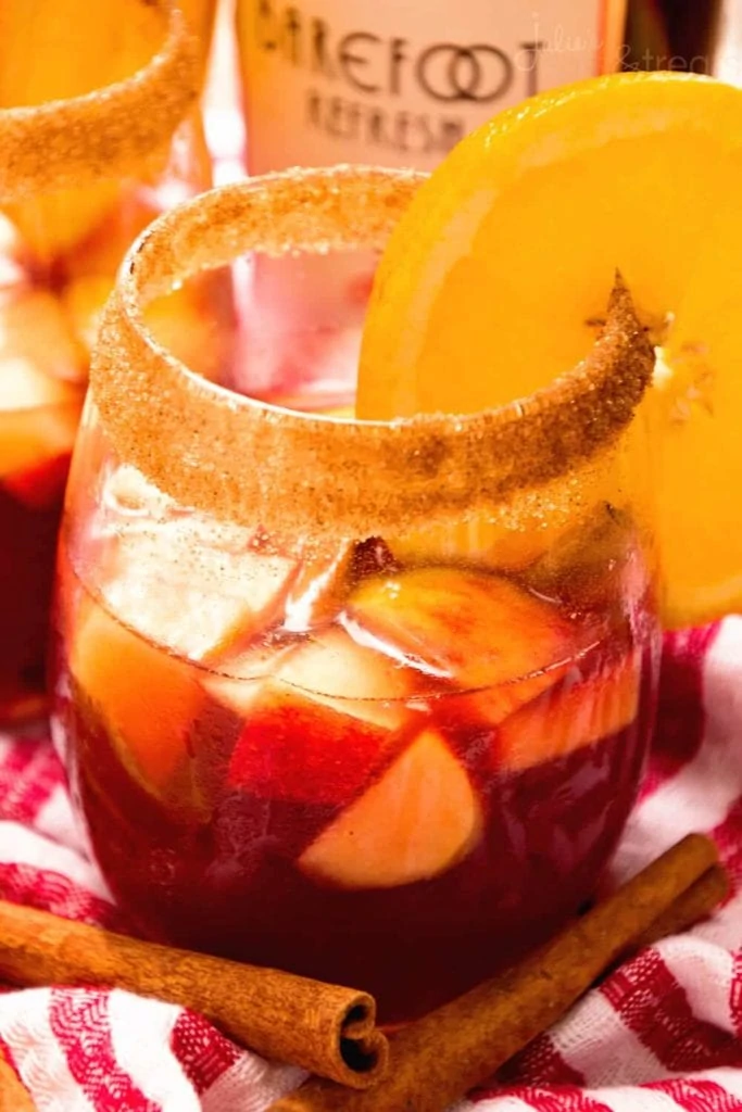 Red Apples and a slice of orange on the rim of the sangria in a cocktail glass.
