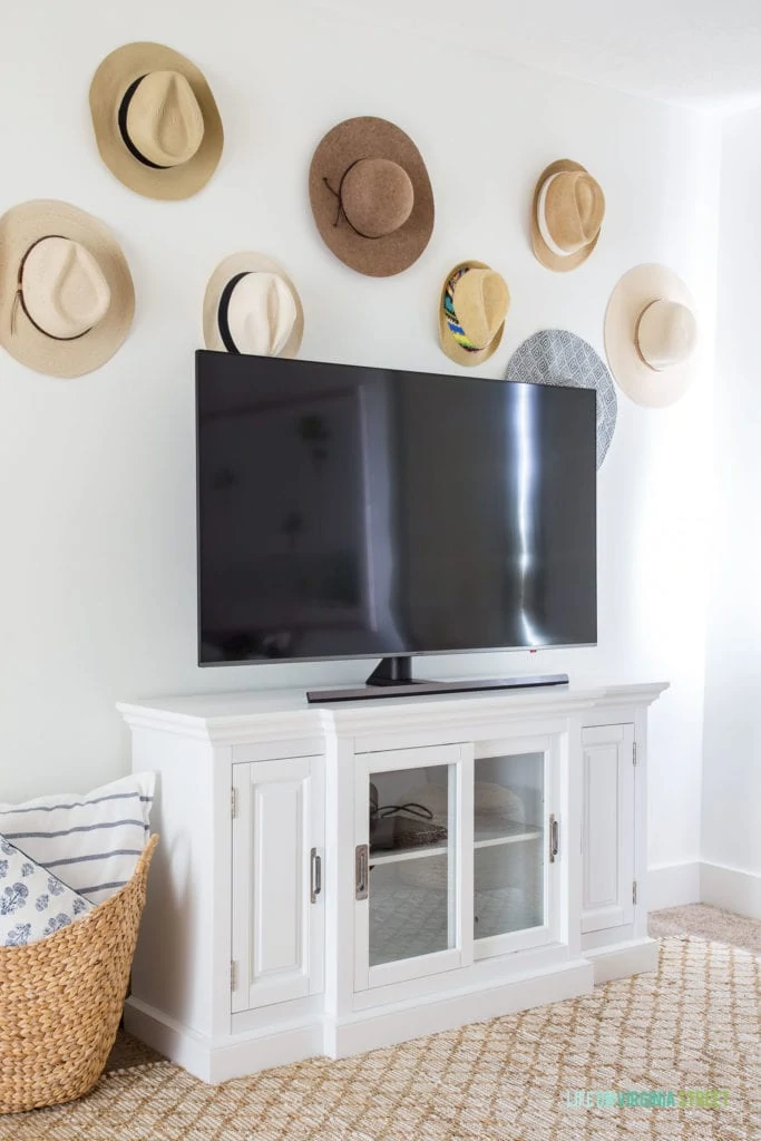 Beachy hats in various neutral shades above the tv in the den.