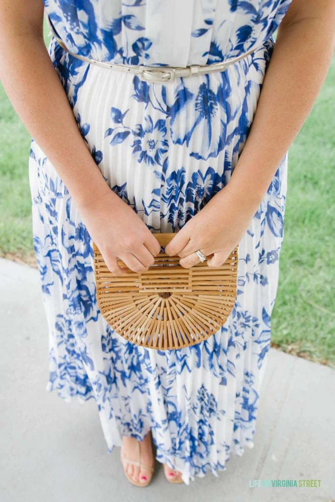 A woman holding a bamboo purse while standing up outside in the blue and white dress.