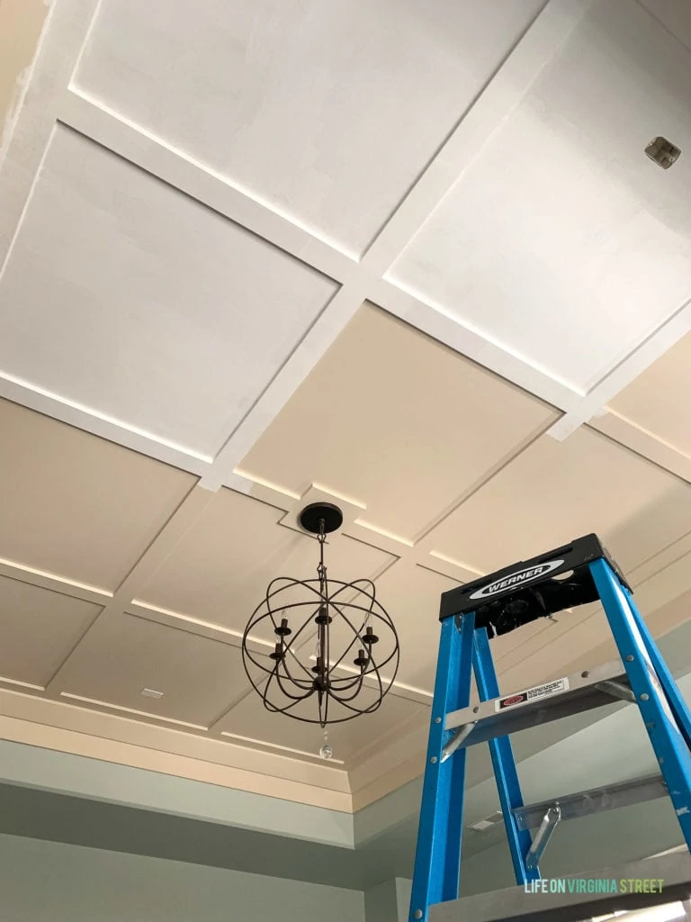 The ceiling being painted white with a ladder reaching to the top of the ceiling.
