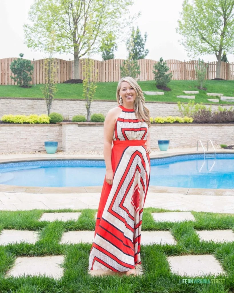 A red and white scarf printed long dress with the model standing in front of the pool.
