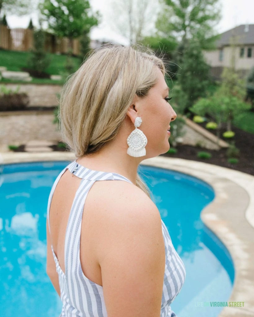 A woman showing the back of the dress that has straps and large white earrings.