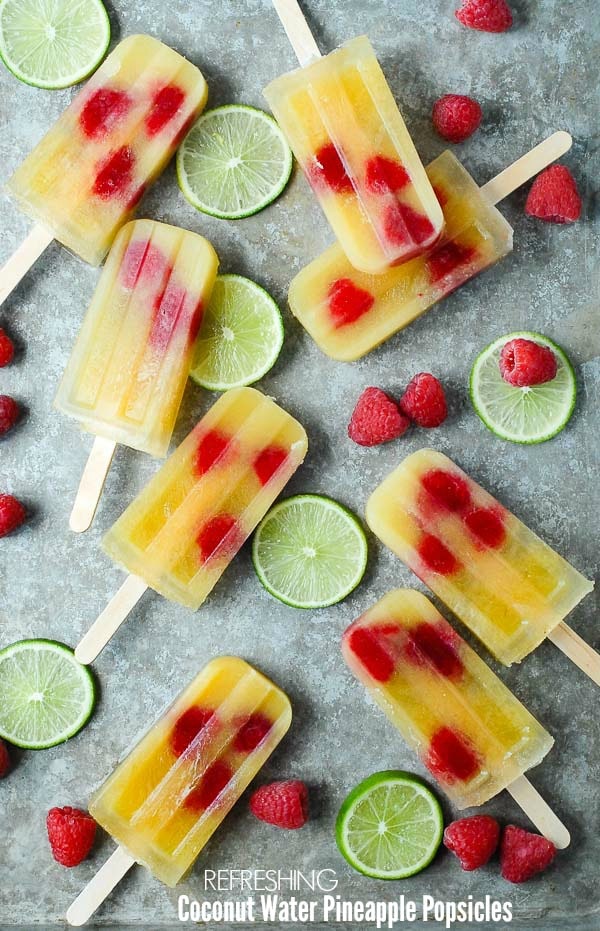 Refreshing Coconut Water Pineapple Popsicle with raspberries in them lying on the counter with cut limes beside them.