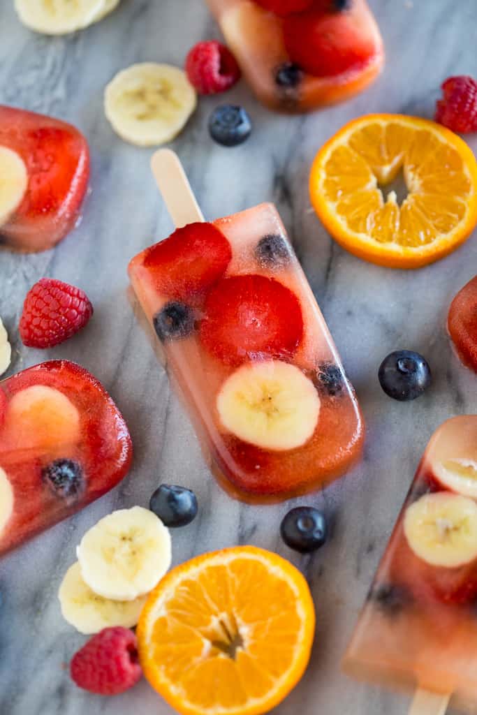 Easy Homemade Fruit Pops with oranges, blueberries and bananas on the counter.