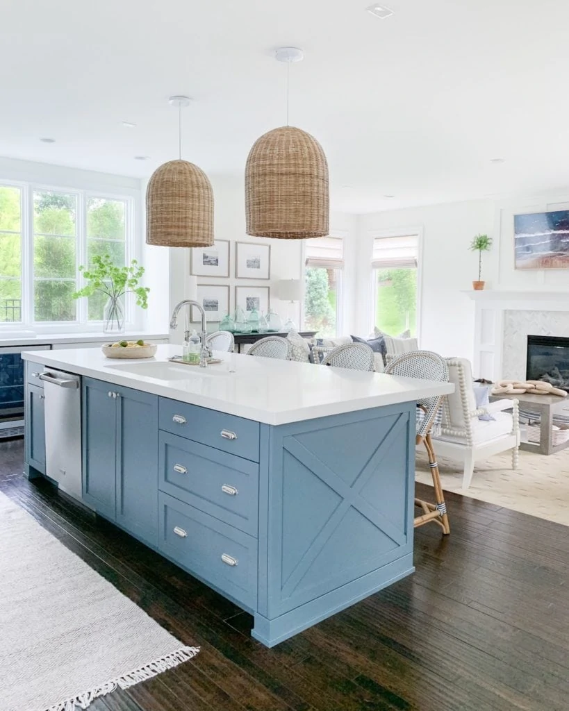 A coastal-inspired summer kitchen with white cabinets, a blue island, basket pendant lights and lots of greenery!