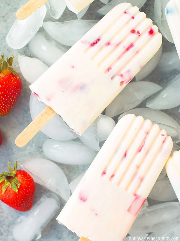 Easy Yogurt Popsicle Recipe with a strawberry beside the popsicles.