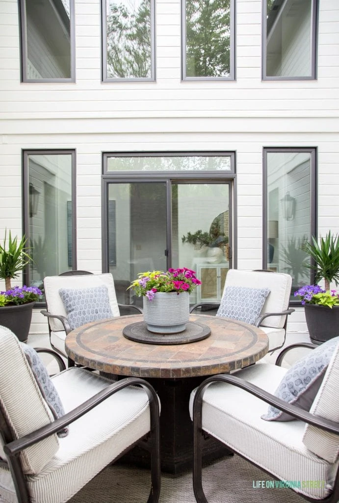 A patio outside of the house with a small table and four chairs and flowers on the table.