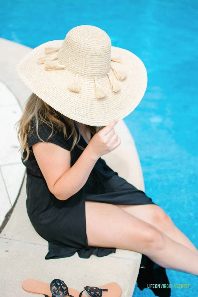 The same person tipping the hat so you cannot see her face, while dipping her feet in the pool.