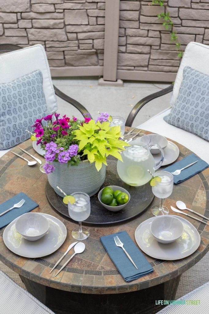 A beautiful outdoor dining tablescape featuring melamine dishes that look like ceramic, linen napkins, block print pillows, striped patio cushions, a gray ceramic flower pot, limes and more!