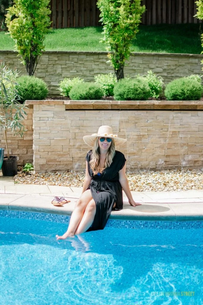 A smiling woman by the pool dipping her feet in.