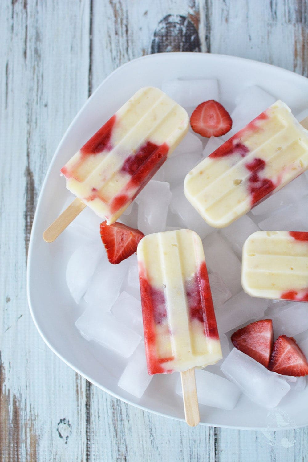 Cheesecake Popsicle with strawberries inside them on a white plate with ice.