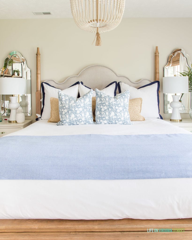 A fabric headboard, beaded chandelier, side tables, mirrors above the side tables in the light guest bedroom.