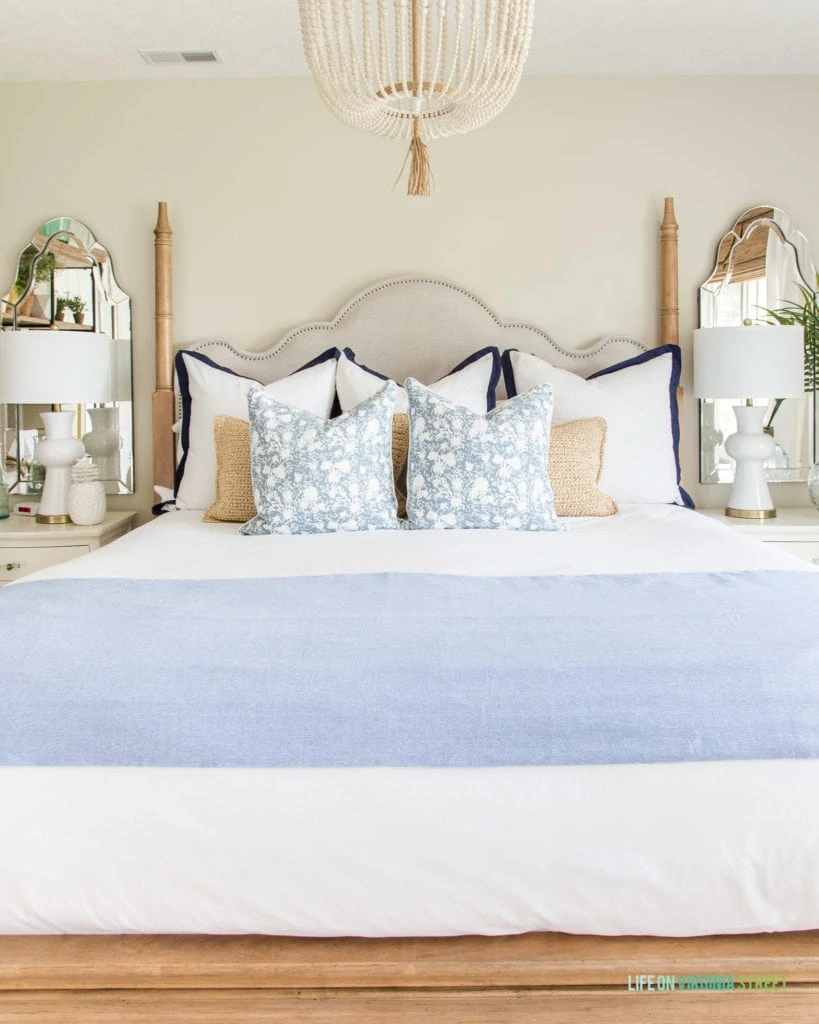 A fabric headboard, beaded chandelier, side tables, mirrors above the side tables in the light guest bedroom.