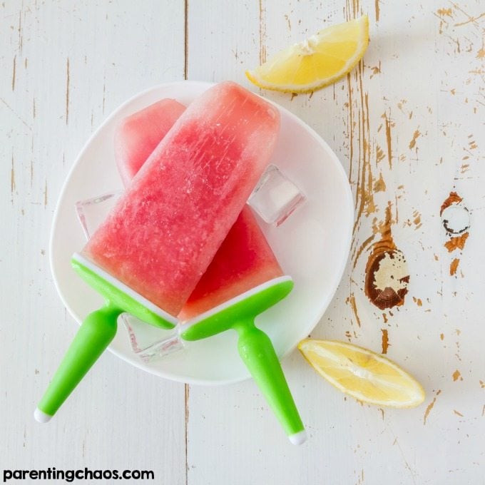 Watermelon Sorbet Popsicles on a white plate with lemons beside it.