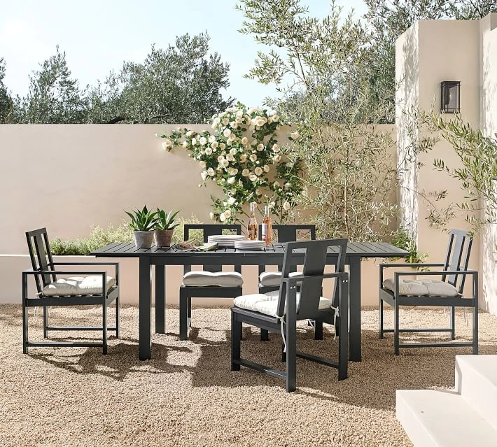 A beautiful courtyard wall idea with white concrete, olive trees, black lanterns, and black out door furniture.