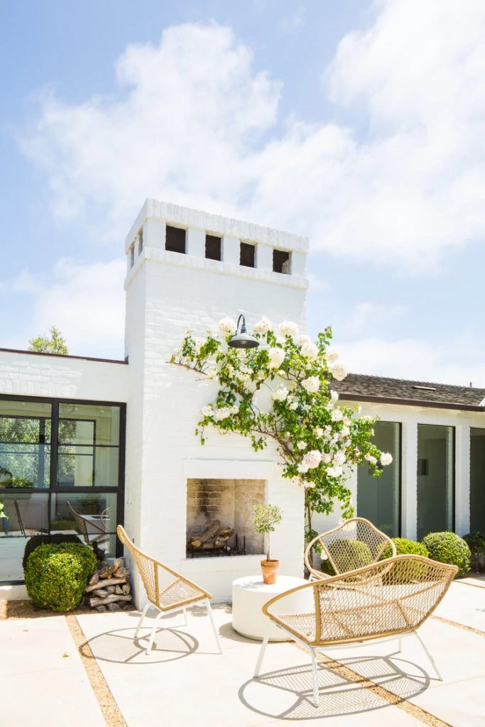 A white brick house and courtyard with black framed windows and doors and a large white outdoor fireplace.