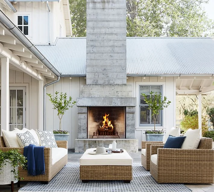 A beautiful outdoor courtyard idea with white house, white windows, woven wicker outdoor furniture, topiary trees, and blue and white accents.