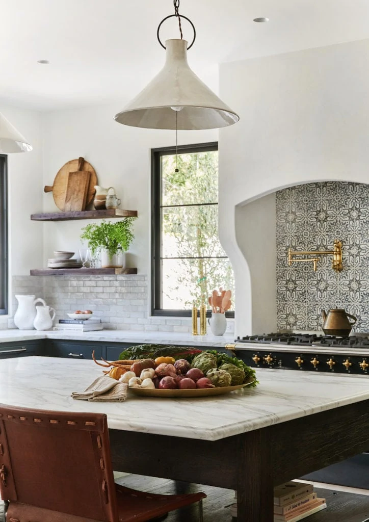 A gorgeous Spanish inspired kitchen with white stucco range, printed tile, black window panes, marble island top, leather chairs and warm accents. Designed by Amber Interiors and photographed by Tessa Neustadt