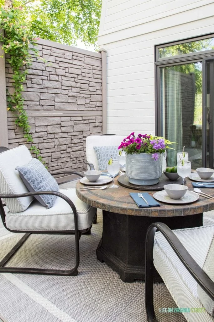 An outdoor patio table set with plates and a large planter in the middle with purple and pink flowers.