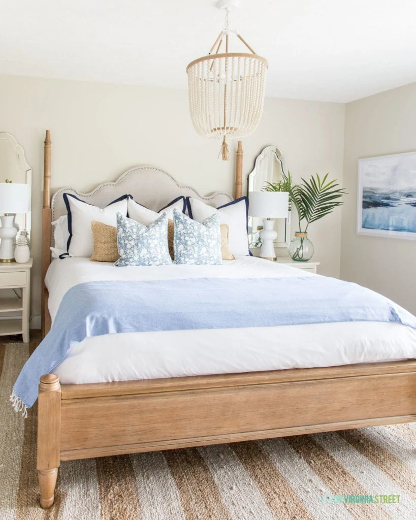 A large beaded chandelier over the neutral bed with two nightstands beside it.