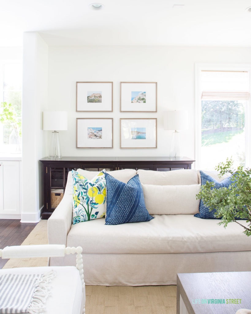 A photo gallery wall in a living room decorated for summer with lemon pillows, faux greenery, and linen sofas.