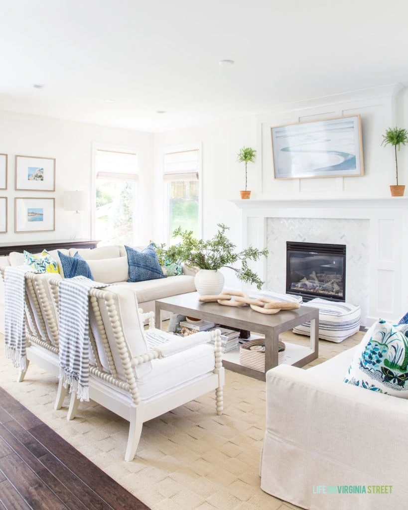 White couches with blue pillows and a striped blanket hanging on the back of the chair. There is a fireplace in the living room as well.