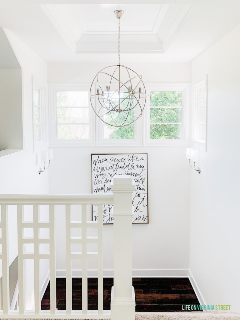 The landing on the stairwell with a chandelier an a painting quote hanging on the wall.