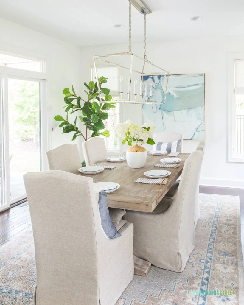 A wooden table with light covered fabric chairs and the hydrangeas in the middle of the table.