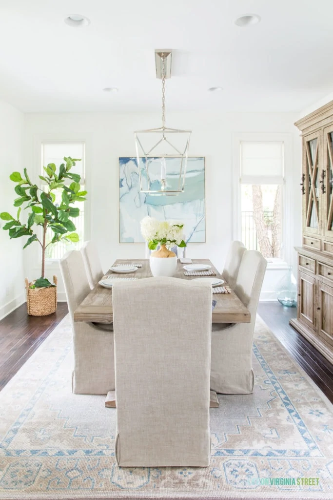 A dining room with Benjamin Moore Simply White walls, linen dining chairs, reclaimed wood dining table, and blue and white accents decorated for summer!