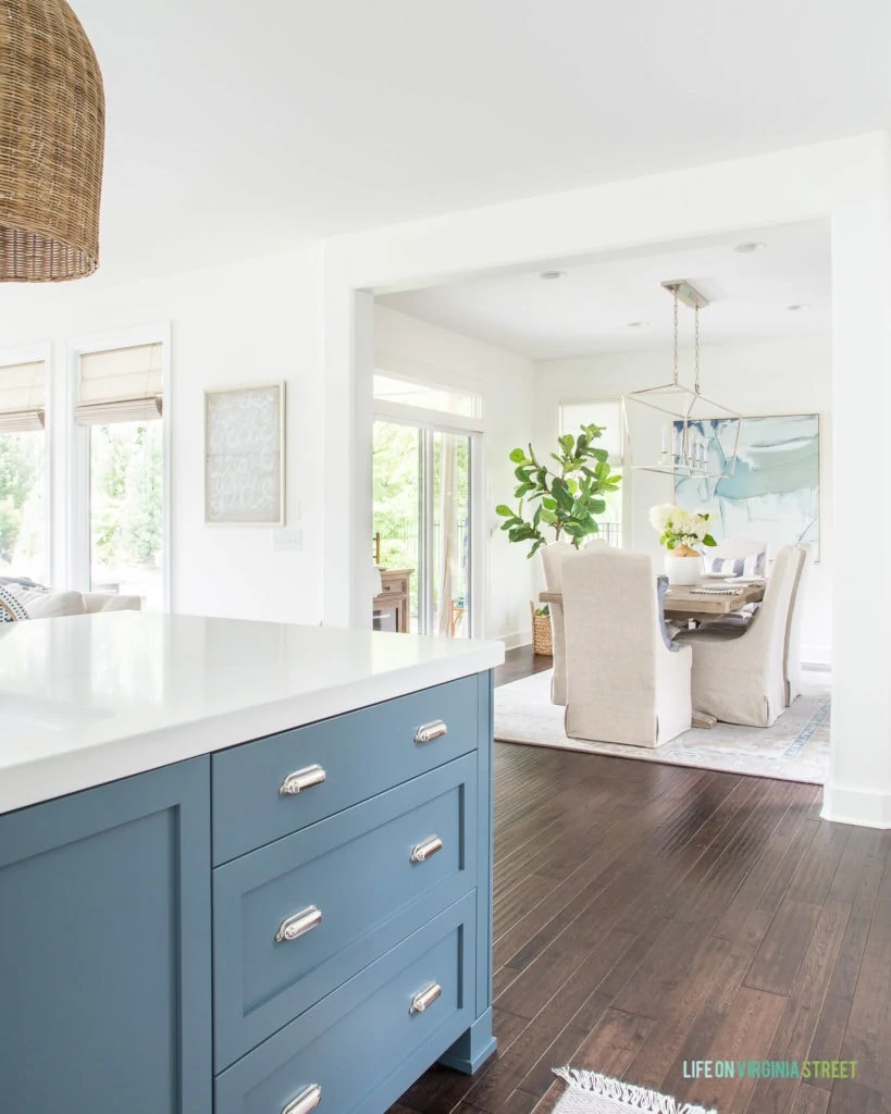 A blue kitchen island (Benjamin Moore Providence Blue) looking into a summer dining room painted Benjamin Moore Simply White. I love the light and airy coastal vibes in this home!