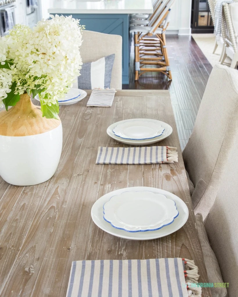 A pretty summer tablescape with blue and white scalloped plates, striped tassel napkins, and limelight hydrangeas in a vase!