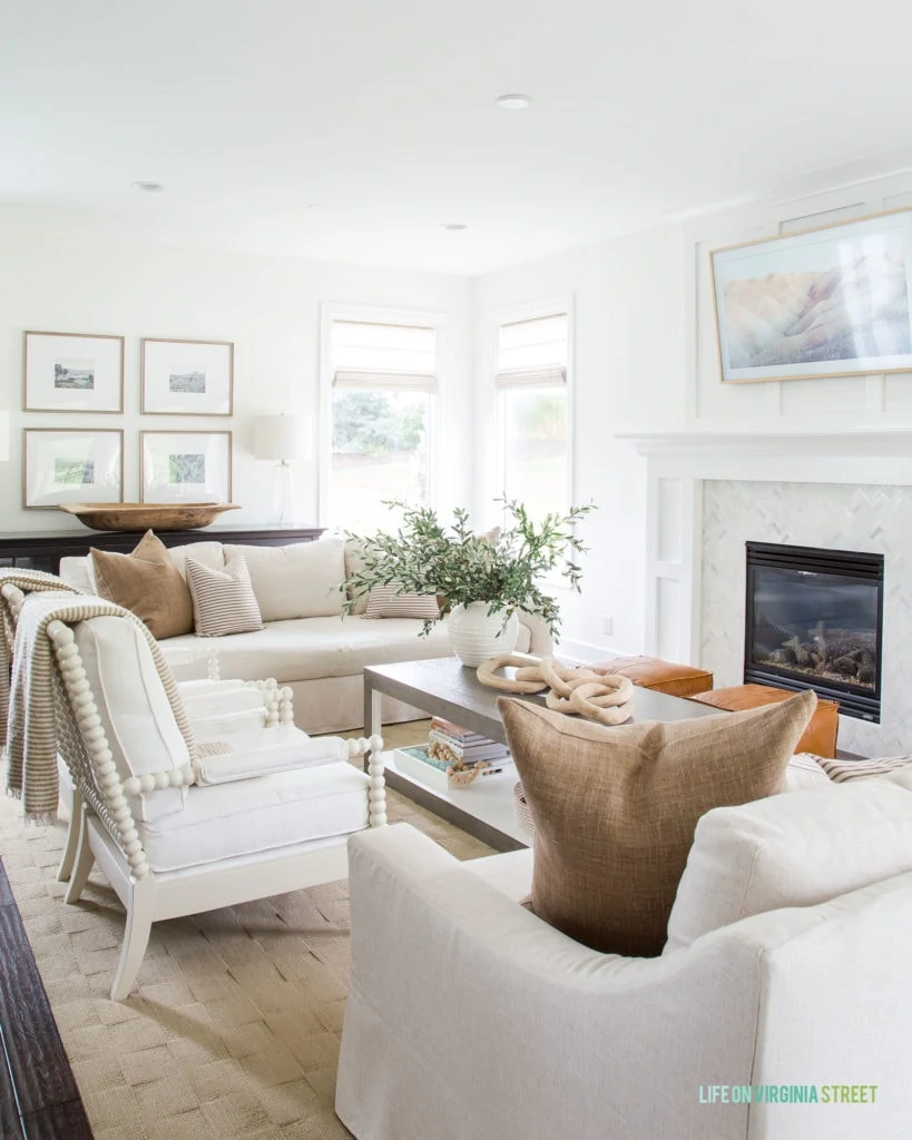 A coastal living room with neutral couches and throw blankets. Plus a white fireplace and mantel.