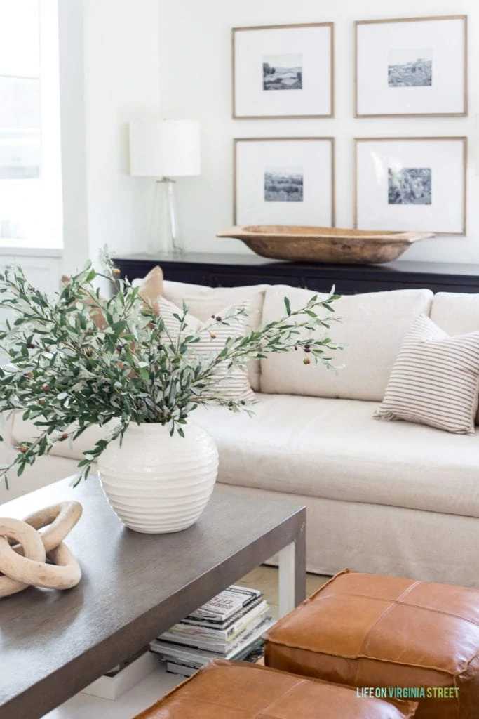A large white ceramic vase filled with faux olive stems in a neutral living room.