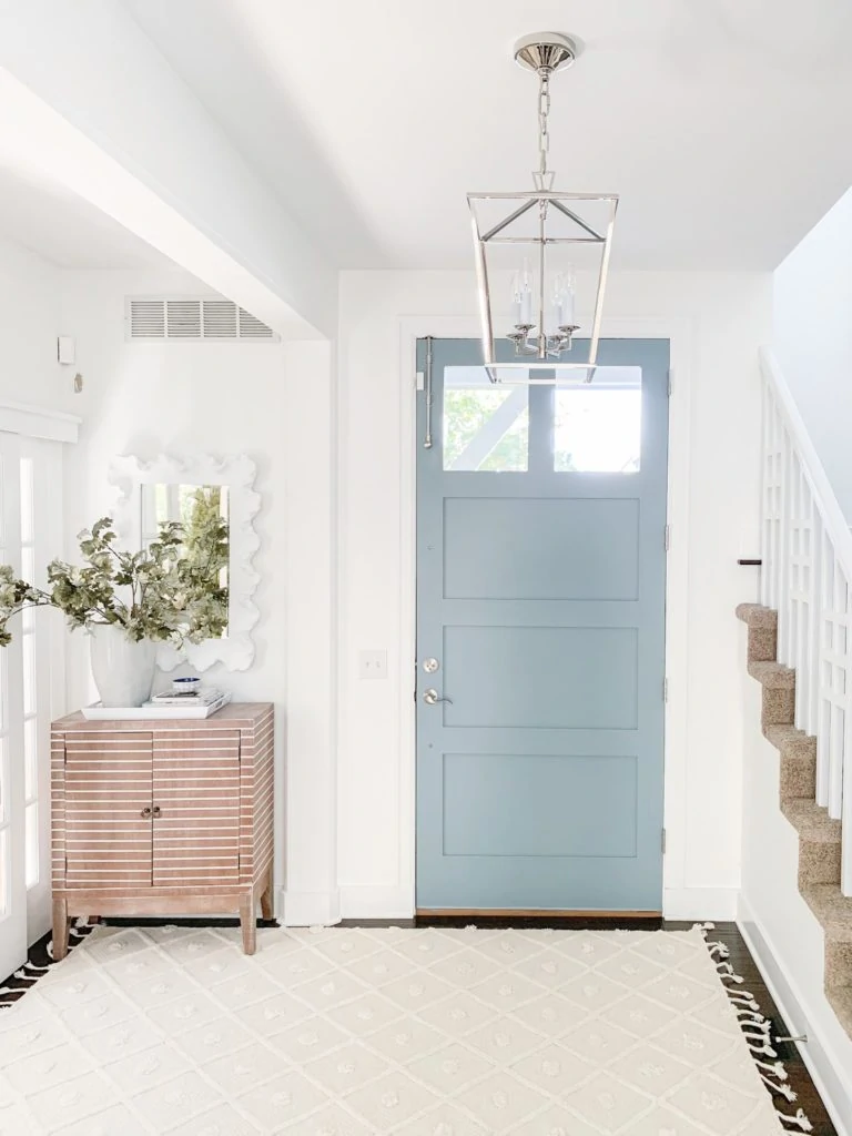 The entryway with a soft blue door and a neutral Pom Pom rug in front of the door.
