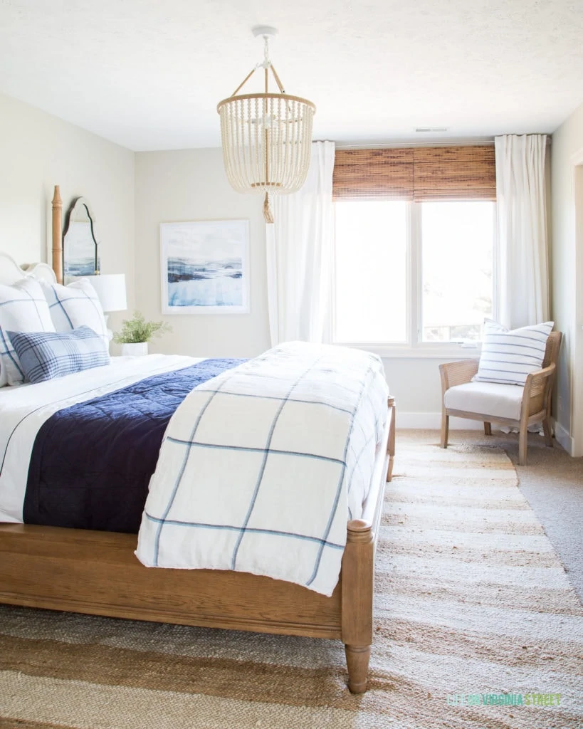 The guest room with greige walls, a wooden bed with a blue and white blanket. There is a beaded chandelier above the bed.