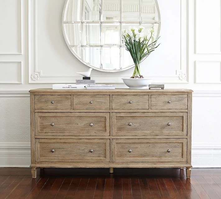 A light wood dresser with multiple drawers and a round silver mirror hung above it.