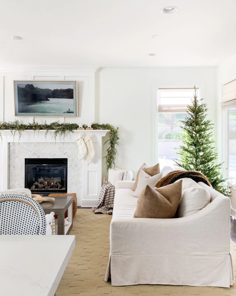 A neutral coastal living room with a Christmas tree in the corner and a mantel decorated.