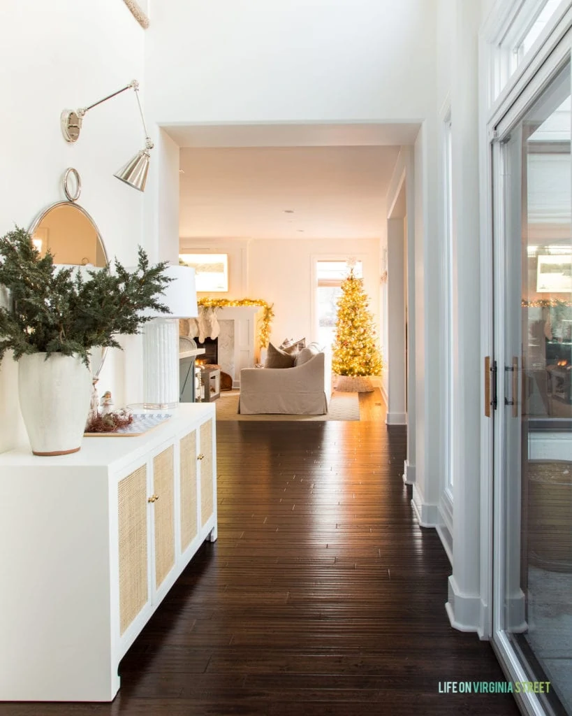 A Christmas hallway with a cane console table, nativity scene, swing arm sconces and a view of the Christmas tree.