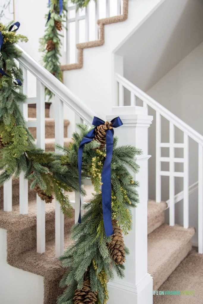 Christmas garland on a white railing tied with navy blue grosgrain ribbon.