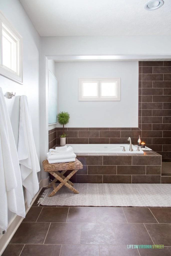 A bathtub in the corner of the bathroom with a small table with towels on it beside the tub.