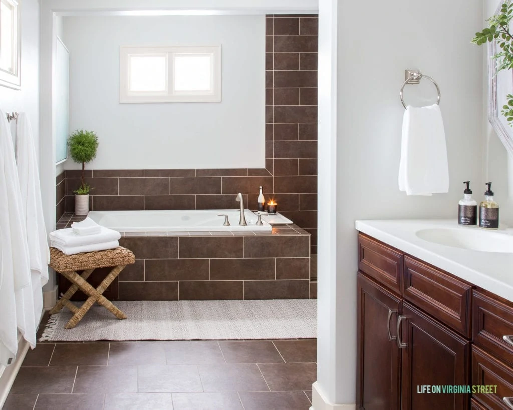 A tiled bathtub with a candle on the side of the tub and half of the sink shown.