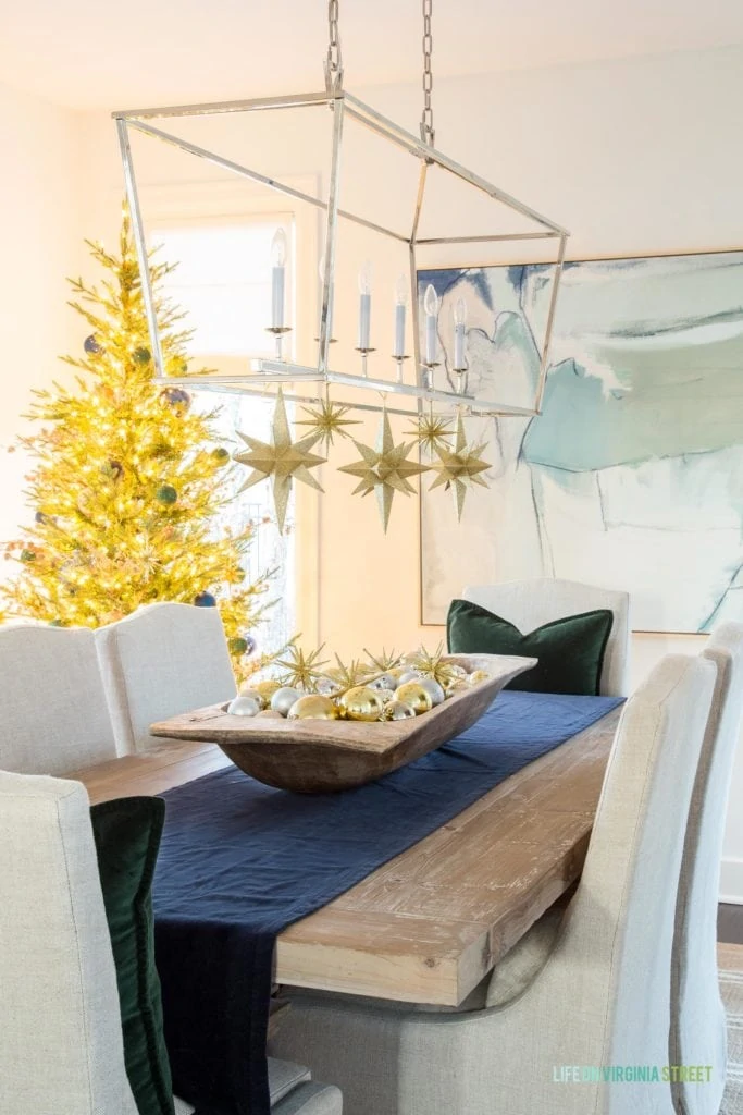 I love these large gold stars hanging from this dining room chandelier, along with the dough bowl filled with ornaments paired with the navy blue and dark green velvet!