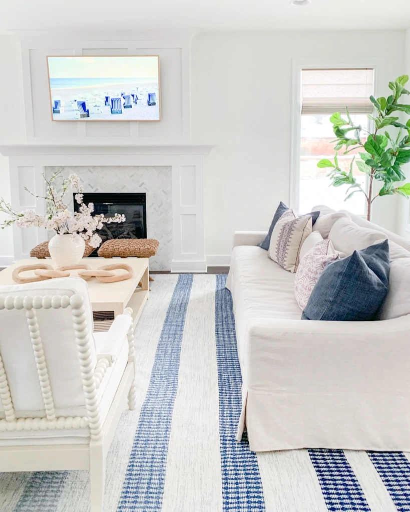 A spring living room with blue and white striped rug, linen sofa, white spindle chairs, faux cherry blossom stems and Etsy spring pillows!
