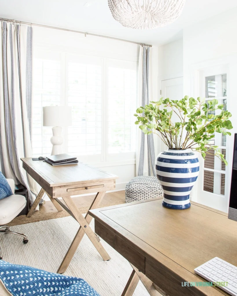 A home office with two wood campaign desks, white walls, wood bead chandelier and a jute rug.